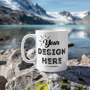 May include: White ceramic mug with a black design that says "Your Design Here" on a rocky surface with a lake and mountains in the background.