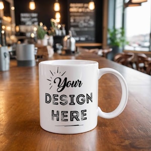 Puede incluir: Taza de caf&eacute; de cer&aacute;mica blanca con un dise&ntilde;o negro que dice "Your Design Here" sobre una mesa de madera.