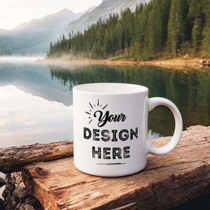May include: White ceramic mug with a black design that says "Your Design Here" on a wooden surface in front of a lake and mountains.