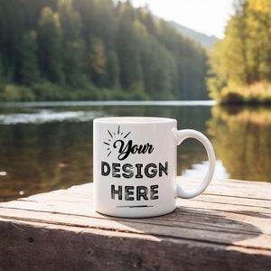 May include: White ceramic mug with a black design that says "Your Design Here" on a wooden surface near a body of water.
