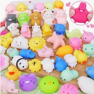 May include: A selection of colourful, squishy toys in animal shapes, such as bunnies, cats, ducks, and bears. The toys are in shades of pink, yellow, blue, green, and white, arranged on a wooden surface.