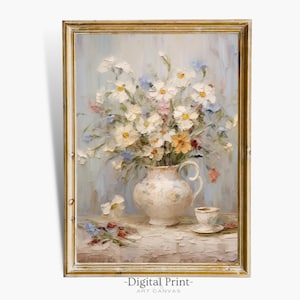 Op de afbeelding: Een schilderij in vintage stijl met een witte vaas gevuld met een boeket witte, gele en blauwe bloemen. De vaas staat op een wit tafelkleed met een klein kopje en schotel ernaast. Het schilderij is ingelijst in een gouden lijst.