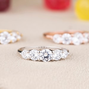 Könnte beinhalten: Drei silberne Ringe mit klaren runden Steinen in einer Reihe. Die Ringe liegen auf einer hellbraunen Oberfläche.