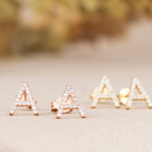 May include: A pair of gold and rose gold initial earrings with a single letter 'A' on each earring. The earrings are set with small, clear cubic zirconia stones.