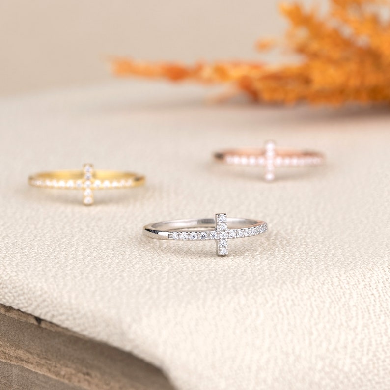 Pu&ograve; includere: Tre anelli delicati con un design a croce incastonati con piccole pietre scintillanti. Gli anelli sono in oro, oro rosa e argento.