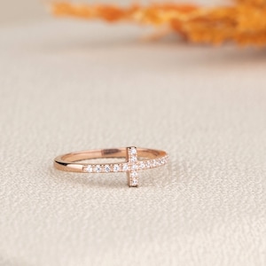 Pu&ograve; includere: Un anello in oro rosa con un piccolo design a croce incastonato con pietre di zircone cubico trasparenti.
