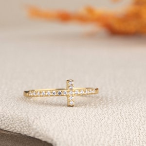 Pu&ograve; includere: Un anello d'oro con un piccolo design a croce incastonato con pietre di zircone cubico trasparenti.
