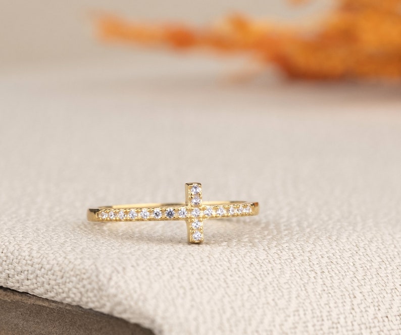 Pu&ograve; includere: Un anello d'oro con un piccolo design a croce incastonato con pietre di zircone cubico trasparenti.