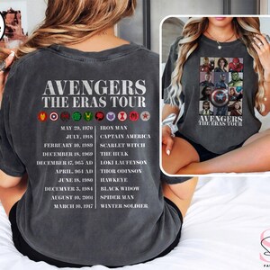 Może przedstawiać: Szary t-shirt w kolorze ciemnego hedera z białym nadrukiem logo Avengers i tekstem "Avengers The Eras Tour". Nadruk zawiera kolaż postaci Avengers i ich odpowiadające im daty trasy koncertowej.