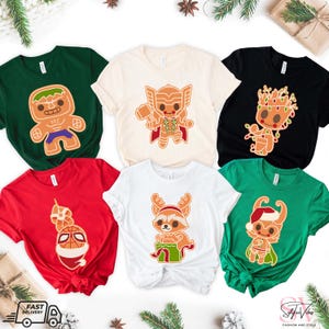 May include: Six different t-shirts featuring various Marvel characters as gingerbread cookies. The characters include Hulk, Thor, Groot, Rocket Raccoon, and Spider-Man. The shirts are in various colors, including green, beige, black, red, and white.
