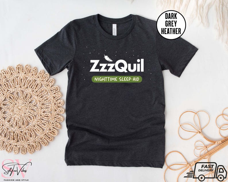 May include: Dark grey heather t-shirt with the text "ZzzQuil NIGHTTIME SLEEP-AID" in white and green. The shirt has a crew neck and short sleeves. A white circle with the words "DARK GREY HEATHER" is in the upper right corner.