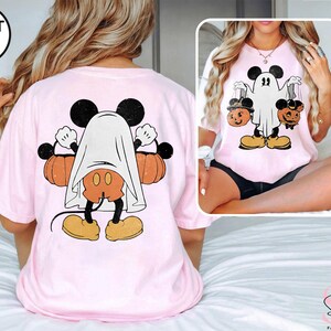 Puede incluir: Una camiseta rosa claro con un gr&aacute;fico de Mickey Mouse disfrazado de fantasma sosteniendo calabazas. El gr&aacute;fico est&aacute; en la parte posterior de la camiseta.
