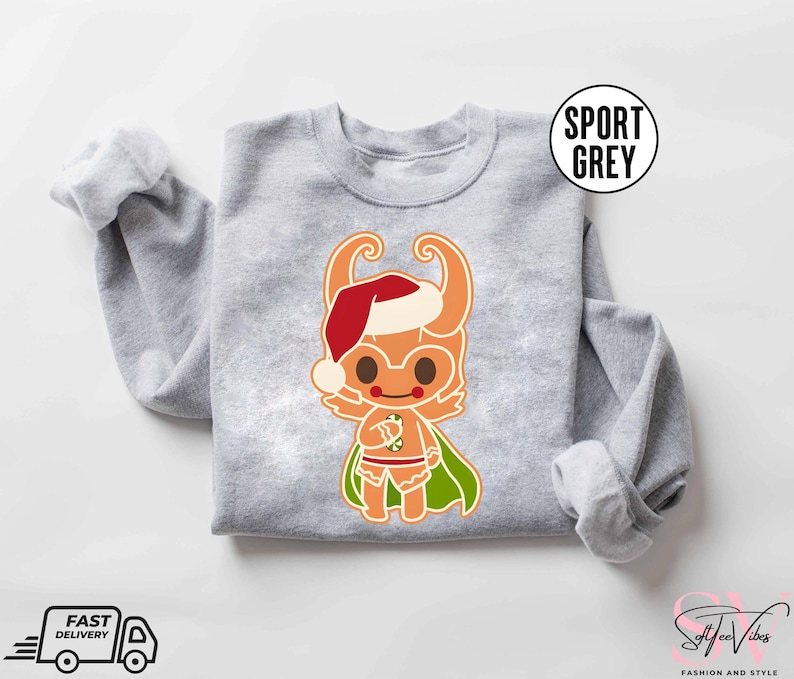 May include: A gray sweatshirt with a Christmas-themed illustration of a gingerbread person wearing a Santa hat and holding a candy cane. The gingerbread person is wearing a green cape and has a red and white striped candy cane.