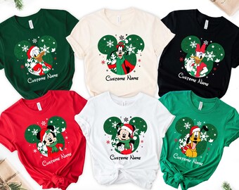 May include: Six Christmas themed t-shirts featuring different Disney characters. The shirts are in various colors, including red, green, white, black, and cream. Each shirt has a green Mickey Mouse ear design with a different character inside. The characters include Mickey Mouse, Minnie Mouse, Donald Duck, Goofy, and Pluto. The text "Custome Name" is printed on each shirt.