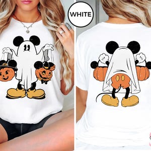 Puede incluir: Camiseta blanca con una ilustraci&oacute;n de estilo vintage de Mickey Mouse vestido de fantasma sosteniendo dos calabazas de jack-o'-lantern. El texto "WHITE" es visible en la esquina superior derecha de la imagen.