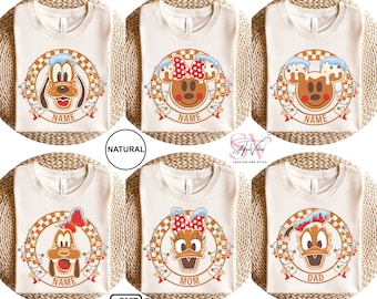 May include: Set of six cream-colored t-shirts with a Christmas theme featuring Mickey Mouse and Pluto characters. The shirts have the words "Name", "Mom", "Dad" printed on them.