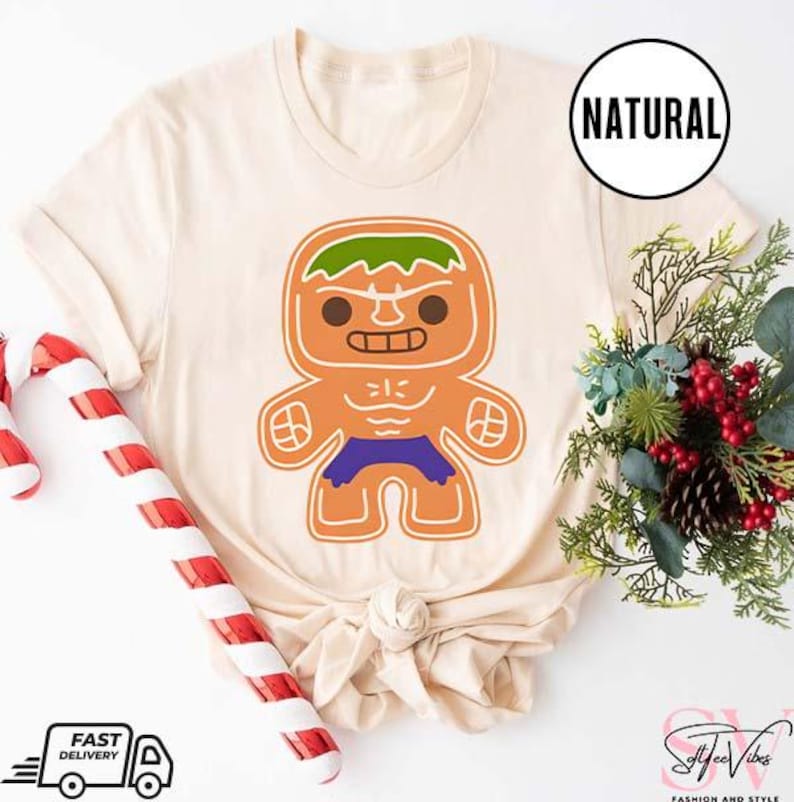 May include: A beige t-shirt with a gingerbread man design. The gingerbread man is green, orange, and purple and resembles the Hulk. The text "NATURAL" is on a white tag.