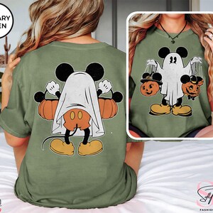 Puede incluir: Una camiseta verde con una ilustraci&oacute;n de estilo vintage de Mickey Mouse vestido de fantasma sosteniendo dos calabazas. El texto "MILITARY GREEN" est&aacute; en un cuadro verde en la esquina superior izquierda de la imagen.