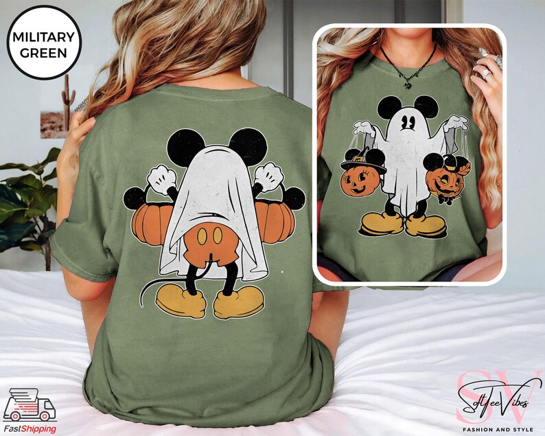 Puede incluir: Una camiseta verde con una ilustraci&oacute;n de estilo vintage de Mickey Mouse vestido de fantasma sosteniendo dos calabazas. El texto "MILITARY GREEN" est&aacute; en un cuadro verde en la esquina superior izquierda de la imagen.