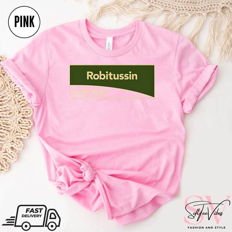May include: Pink t-shirt with the word "Robitussin" in white text on a dark green rectangle. The text "COUGH RELIEF" is below. The shirt has rolled-up sleeves and a knot at the bottom. A "Pink" circle is in the upper left.