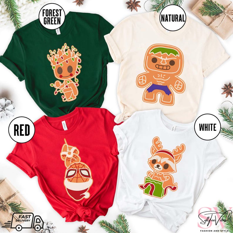 May include: Four different t-shirts with Christmas-themed designs featuring characters from popular movies and TV shows. The shirts are in red, green, white, and natural colors. The designs include a gingerbread man version of the Hulk, a gingerbread man version of Rocket Raccoon, a gingerbread man version of Spider-Man, and a gingerbread man version of Groot.