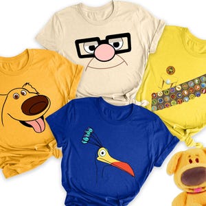 Könnte beinhalten: Vier T-Shirts mit Figuren aus dem Animationsfilm Obendrauf. Die Shirts sind gelb, beige, blau und gelb. Die Figuren sind Dug, Kevin, Russell und ein Scout-Abzeichen-Design.