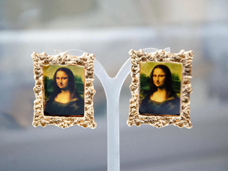 May include: A pair of gold-tone earrings with a textured frame, each featuring a miniature painting of the Mona Lisa.