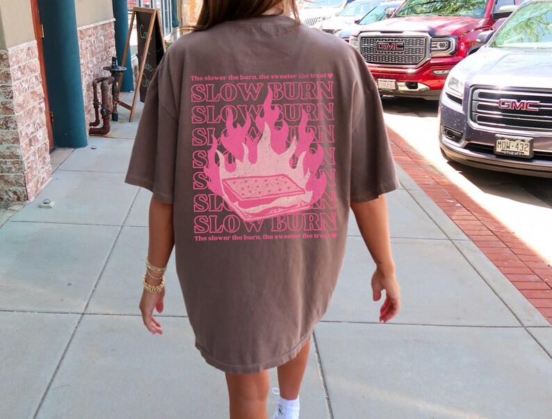 May include: A brown t-shirt with a pink graphic of a burning s'more and the text "The slower the burn, the sweeter the treat" and "SLOW BURN" repeated multiple times.