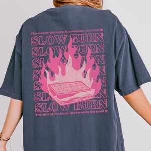 May include: A dark blue t-shirt with a pink graphic of a burning s'more and the text "The slower the burn, the sweeter the treat" and "SLOW BURN" repeated multiple times.