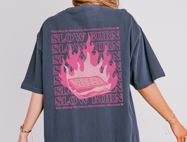 May include: A dark blue t-shirt with a pink graphic of a burning s'more and the text "The slower the burn, the sweeter the treat" and "SLOW BURN" repeated multiple times.