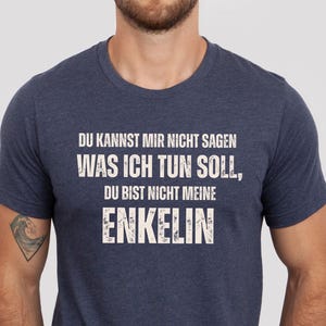 Könnte beinhalten: Heather-Navy-T-Shirt mit weißem Text. Der Text lautet: "DU KANNST MIR NICHT SAGEN WAS ICH TUN SOLL, DU BIST NICHT MEINE ENKELIN". Das Shirt hat einen Rundhalsausschnitt und kurze Ärmel. Die Farbe ist Heather Navy.