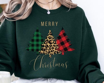 May include: A dark green sweatshirt with the words "MERRY Christmas" in gold script. The design features three Christmas trees with plaid, leopard print, and buffalo check patterns. The word "green" is written in white at the bottom right.