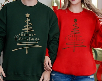 May include: Two sweatshirts, one green and one red, feature a gold and green Christmas tree design with the words "Merry Christmas." The green sweatshirt is paired with a person wearing a bracelet and a ring. The red sweatshirt is paired with a person wearing blue jeans.