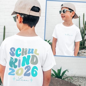Könnte beinhalten: Ein weißes T-Shirt mit einer bunten Grafik auf der Rückseite, die den Text "SCHULKIND 2026" in einer geschwungenen Schrift, ein Bleistift-Symbol und den Namen "Leon" in Schreibschrift zeigt. Auf der Vorderseite steht der Name "Leon" in kleiner Schrift.