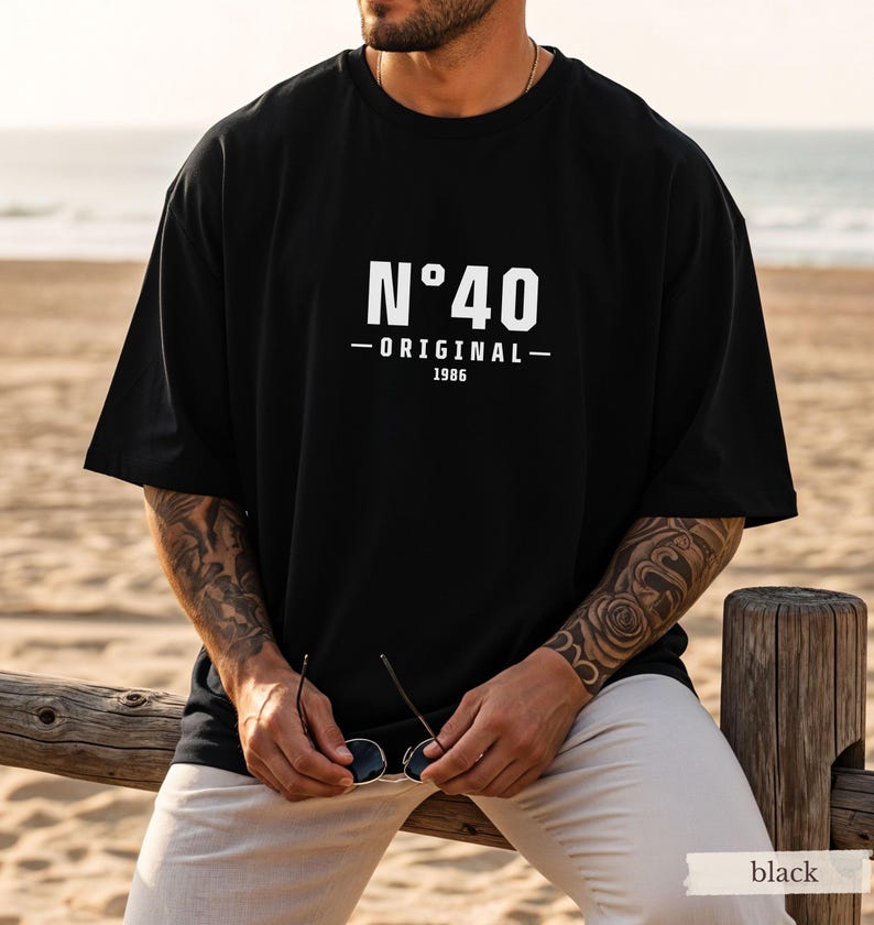 May include: A black short-sleeved t-shirt featuring white text on the chest that reads N&deg;40 ORIGINAL 1986. The shirt has a crew neckline and a loose, relaxed fit. The design is centered on the front of the garment in a clean, bold font.