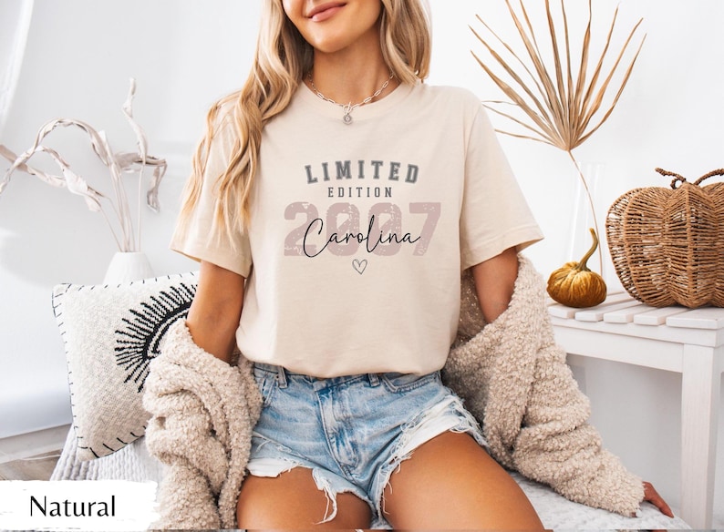 K&ouml;nnte beinhalten: Beiges T-Shirt mit dem Text "LIMITED EDITION 2007 Carolina" in verschiedenen Schriftarten und Farben. Das Shirt wird mit Jeansshorts und einer cremefarbenen Strickjacke kombiniert. Der Look ist l&auml;ssig und entspannt.