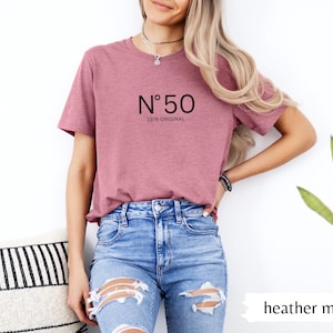 May include: Heather mauve t-shirt with the text "N&ordm; 50 1976 ORIGINAL" in black. The model is wearing blue jeans. The shirt is a solid color and has a round neckline. The shirt is made of a soft, comfortable material.