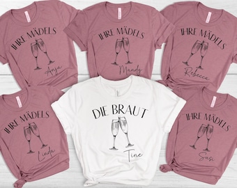 May include: A collection of mauve and white t-shirts with black text and champagne glass illustrations. The shirts say "IHRE MÄDELS" and "DIE BRAUT" with names like Anja, Mandy, Rebecca, Linda, Tine, and Susi. Perfect for a bachelorette party.