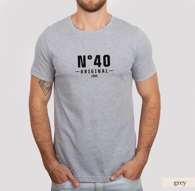May include: A heather grey short-sleeved t-shirt featuring black text on the chest that reads N&deg;40 ORIGINAL 1986. The garment has a crew neckline and a standard fit, constructed from a soft, lightweight fabric with a visible heathered texture.