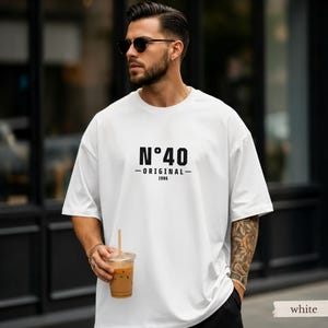 May include: A white short-sleeved t-shirt featuring black text on the chest that reads N&deg;40, ORIGINAL, and 1986. The shirt has a crew neckline and a loose, relaxed fit. The design is centered on the front of the garment in a bold, sans-serif font.