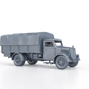 Op de afbeelding: Een grijs model van een vintage militaire vrachtwagen met een canvas zeil dat de laadbak bedekt. De vrachtwagen heeft een grote, afgeronde grille aan de voorkant en een enkele cabine.
