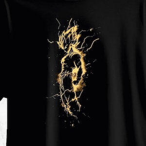 Puede incluir: Camiseta negra con una ilustración dorada de una figura musculosa con pelo puntiagudo y rayos. La obra de arte tiene una sensación dinámica y enérgica, con un enfoque en la silueta y el poder del personaje.