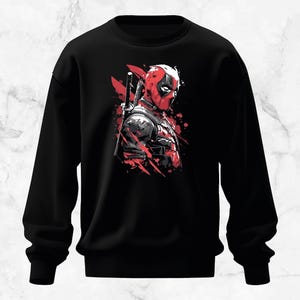 Puede incluir: Sudadera negra con un gr&aacute;fico de Deadpool en rojo y negro. La ilustraci&oacute;n muestra a Deadpool con su m&aacute;scara, una espada en la espalda y salpicaduras rojas.
