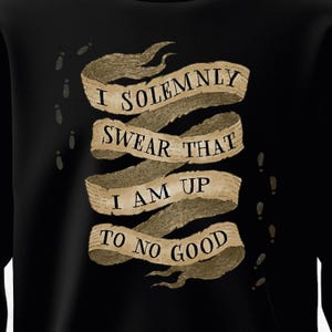 May include: A black long-sleeve shirt featuring a beige, multi-layered parchment-style ribbon graphic. The text "I SOLEMNLY SWEAR THAT I AM UP TO NO GOOD" is printed in black serif font across the ribbon, surrounded by small dark footprints.