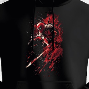 Pode incluir: Moletom preto com um gráfico marcante de uma figura mascarada em ação, empunhando uma espada. O design usa um esquema de cores vermelho e preto arrojado, com respingos de vermelho criando um efeito dramático. O moletom tem um bolso frontal e um capuz com cordão.