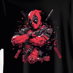 Pode incluir: Camiseta preta com um gráfico de Deadpool em um traje vermelho e preto, com os braços cruzados. A ilustração é em estilo de quadrinhos com efeitos de respingos de tinta vermelha e duas katanas.