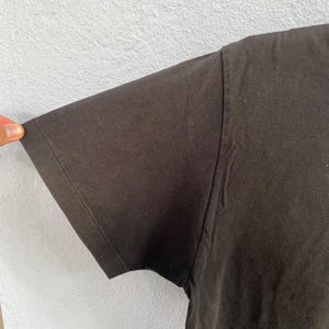 Puede incluir: Primer plano de una manga de camiseta negra. La manga est&aacute; hecha de una tela oscura y suave y est&aacute; cosida a lo largo del borde. El fondo es una pared gris claro.