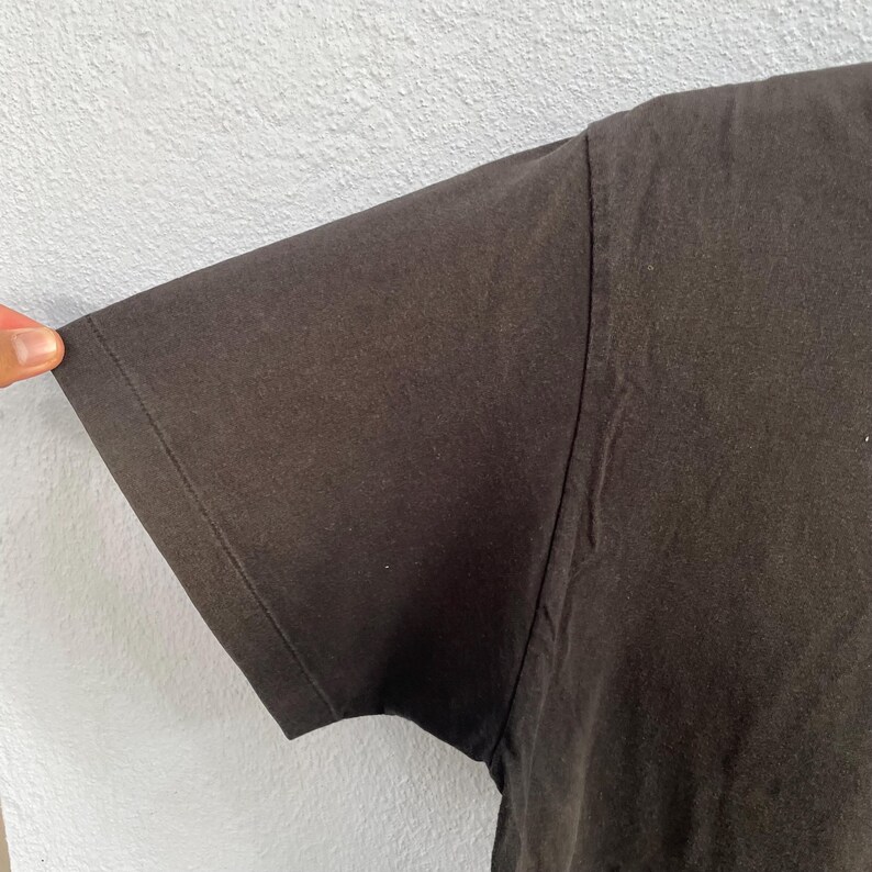 Puede incluir: Primer plano de una manga de camiseta negra. La manga est&aacute; hecha de una tela oscura y suave y est&aacute; cosida a lo largo del borde. El fondo es una pared gris claro.