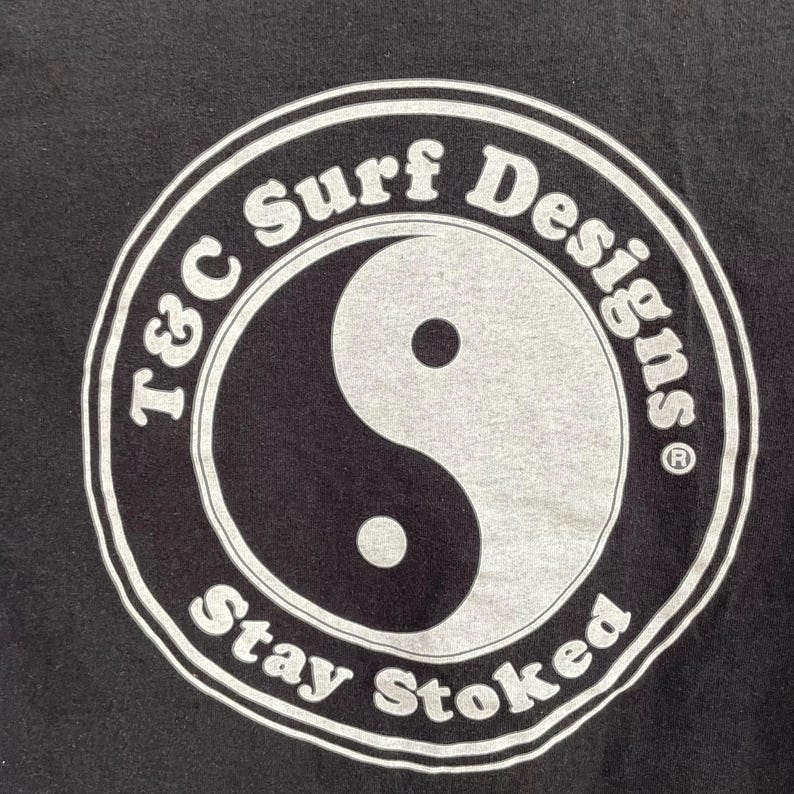 Puede incluir: Gr&aacute;fico negro con un s&iacute;mbolo de yin-yang y las palabras "T&C Surf Designs" y "Stay Stoked" en un dise&ntilde;o circular. El yin-yang est&aacute; dividido entre negro y gris. El texto es blanco.