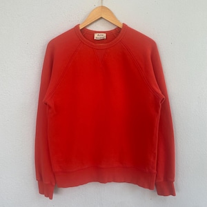 Op de afbeelding: Een effen rode sweatshirt met lange mouwen, hangend aan een houten hanger. De sweatshirt heeft een ronde hals en een klein label met de tekst "Acne Studios". Het kledingstuk is gemaakt van een zacht materiaal.